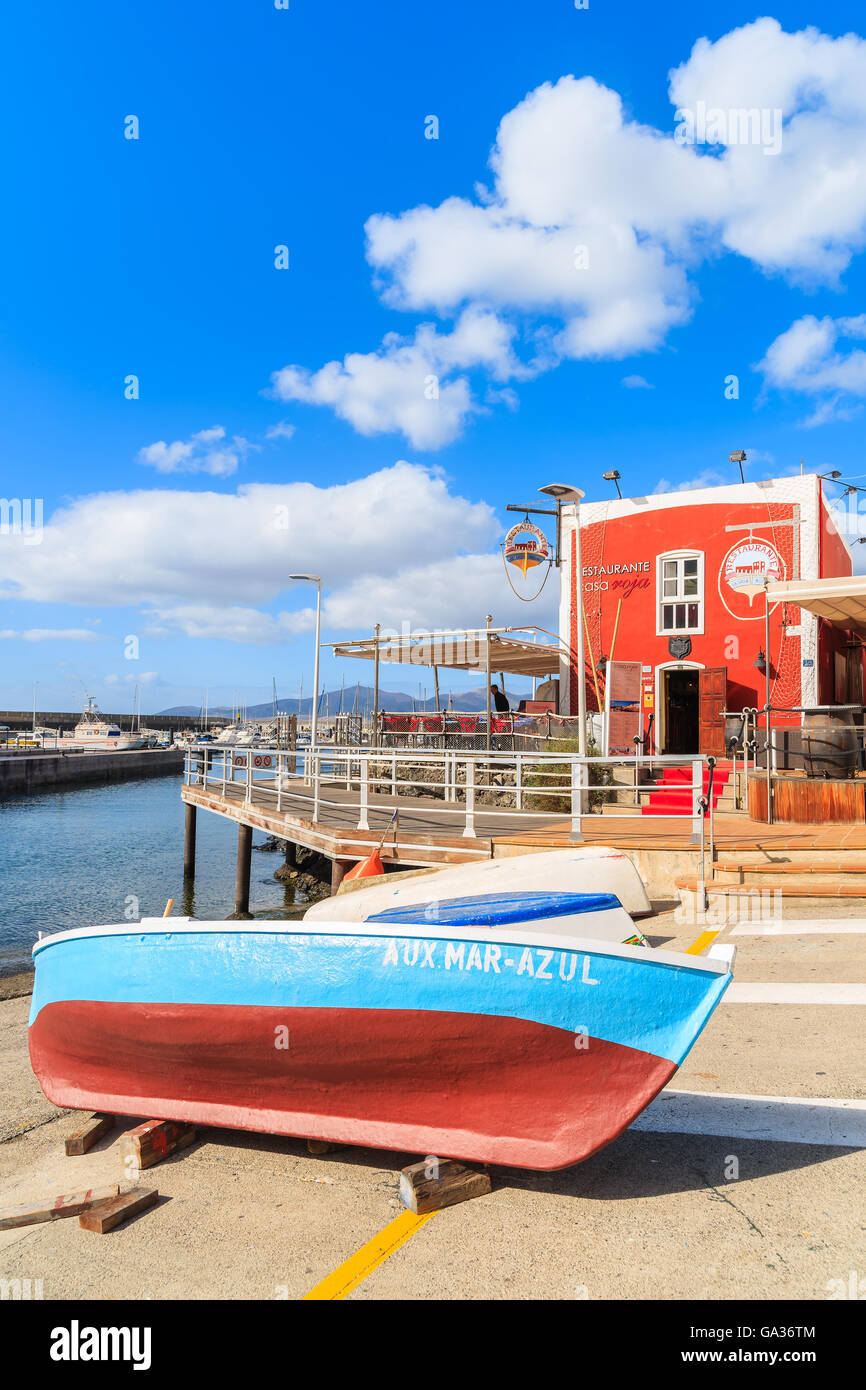 PUERTO DEL CARMENT PORT, LANZAROTE - JAN 17, 2015: colorful fishing boat in front of red restaurant building in Puerte del Carmen port. This town is popular holiday destination on Lanzarote island. Stock Photo