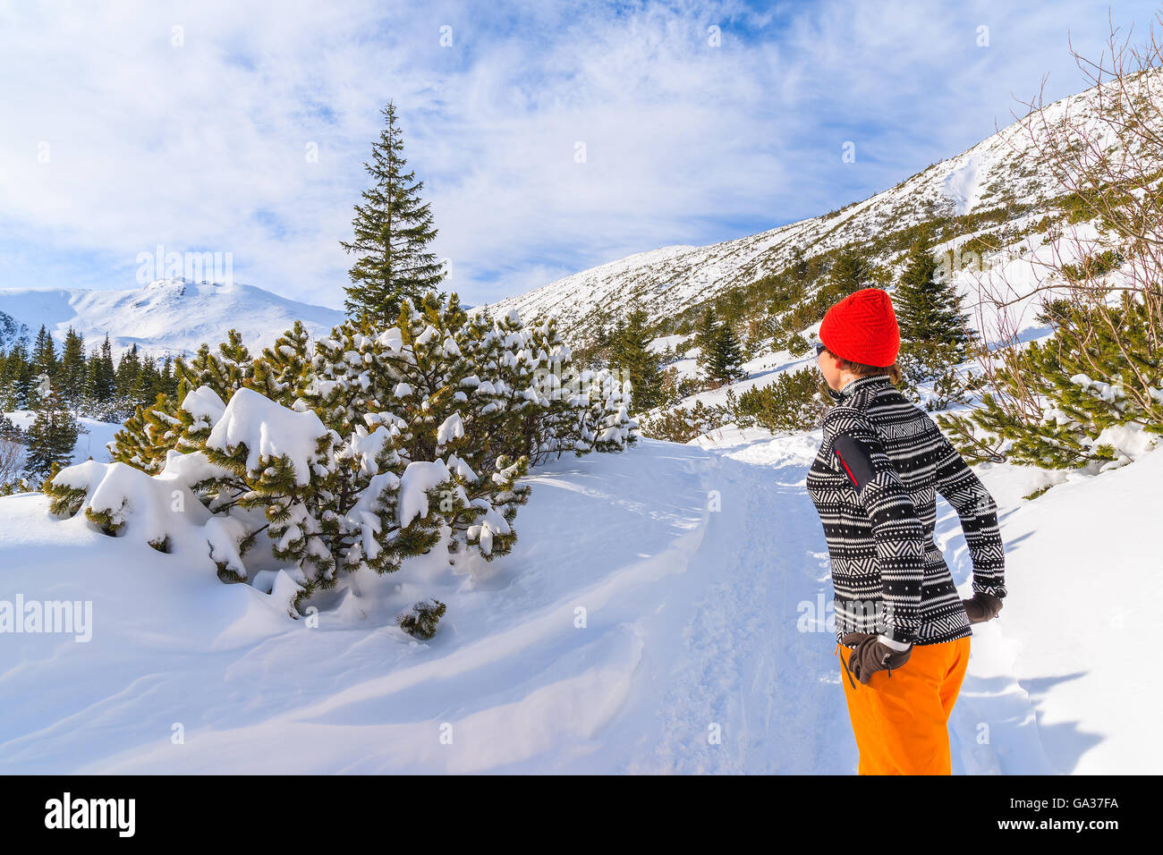 Young woman tourist in sweater, orange pants and red hat on winter path in Gasienicowa valley, Tatra Mountains, Poland Stock Photo