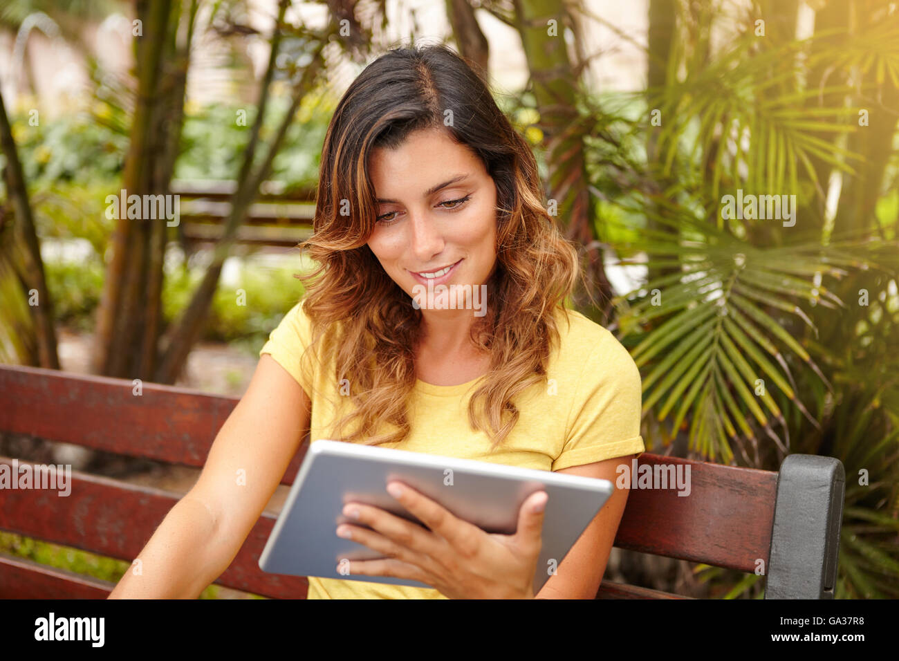 Young lady with medium-length hair toothy smiling while using tablet outdoors Stock Photo