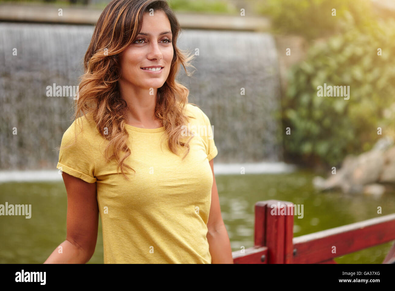 Young lady with medium-length hair smiling while standing near park lake Stock Photo