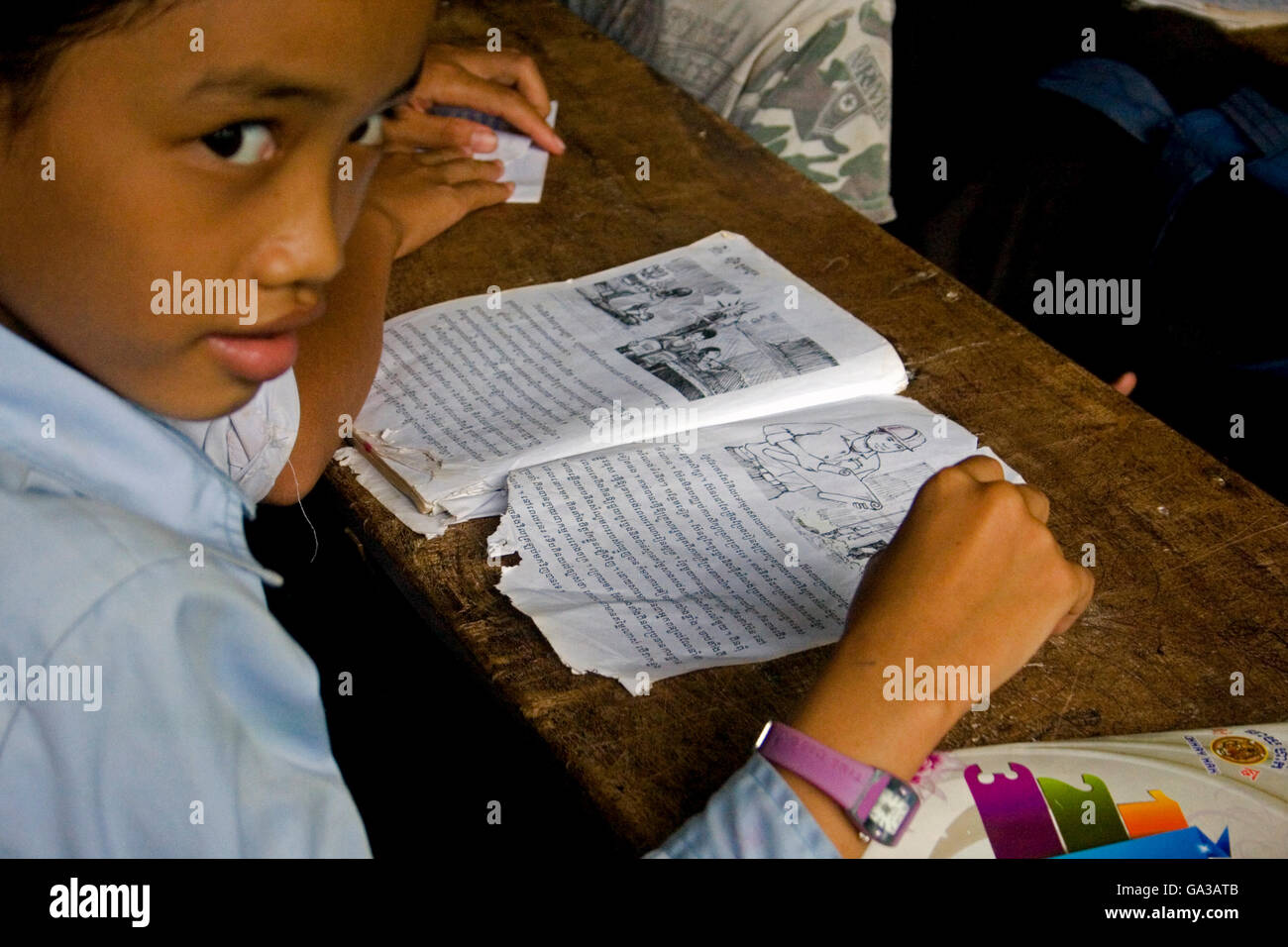 A young Asian girl is sitting at a desk studying at a primary school in Chork Village, Cambodia. Stock Photo