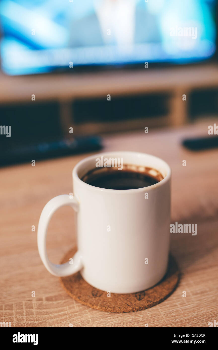 Morning coffee in white cup, shallow dof, television in background, selective focus Stock Photo