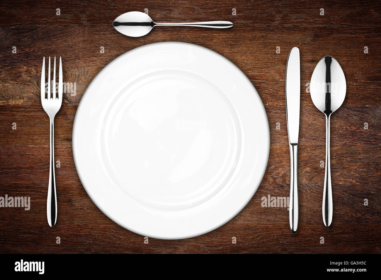place setting with empty dish fork spoon and knife on wooden background Stock Photo