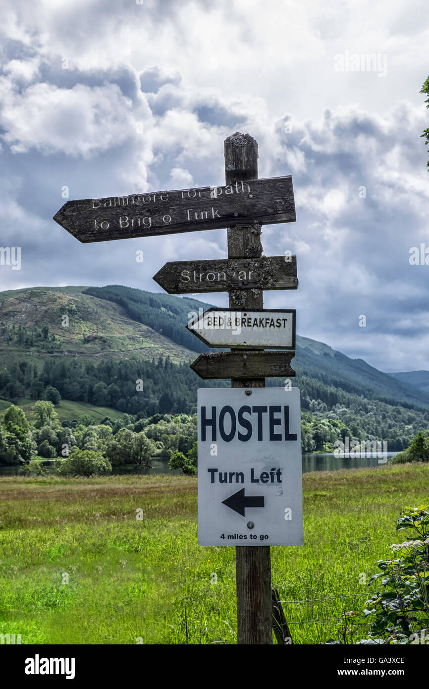 Old wooden signpost at Balquhidder, Scotland with Loch Voil and mountains in the background Stock Photo