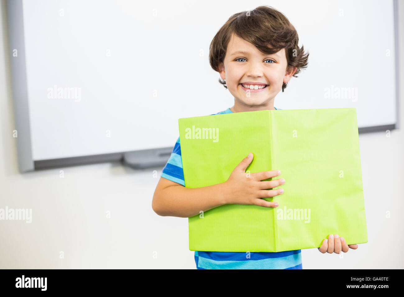 Portrait of schoolboy standing with book in classroom Stock Photo - Alamy