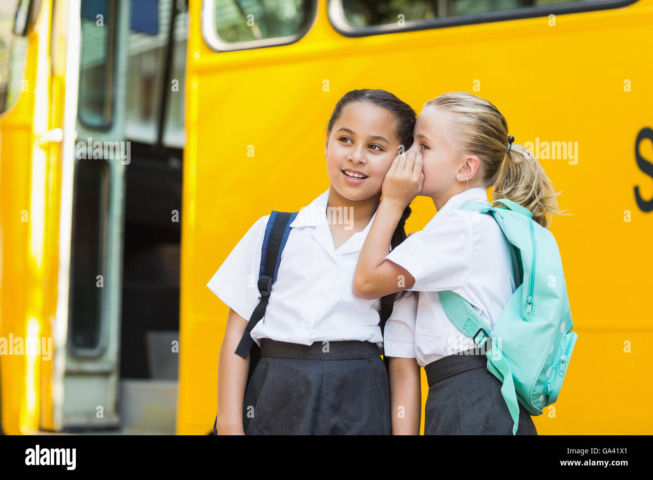 Smiling schoolgirl whispering in her friend's ear Stock Photo