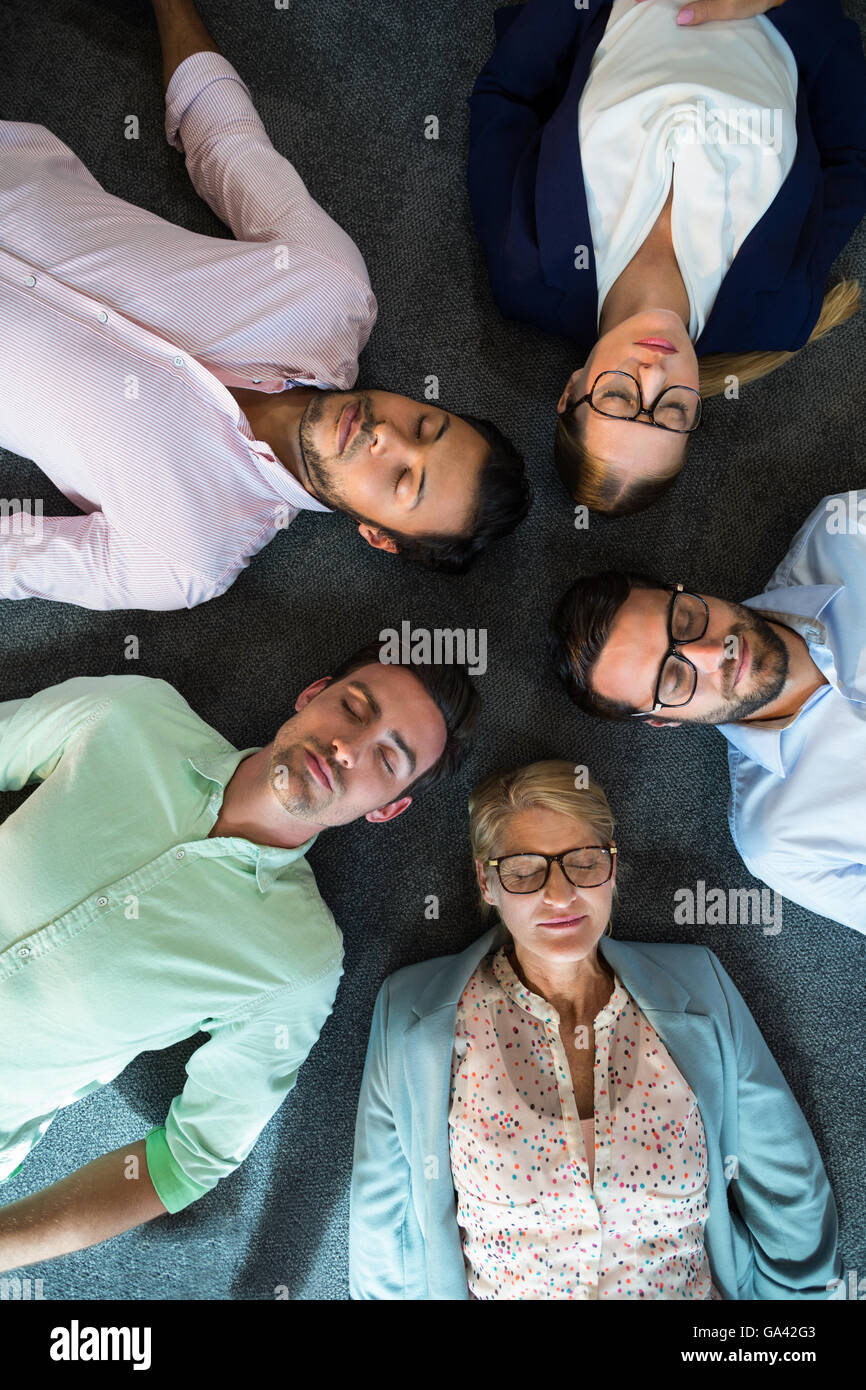 Business team with eyes closed lying on the floor with head together Stock Photo