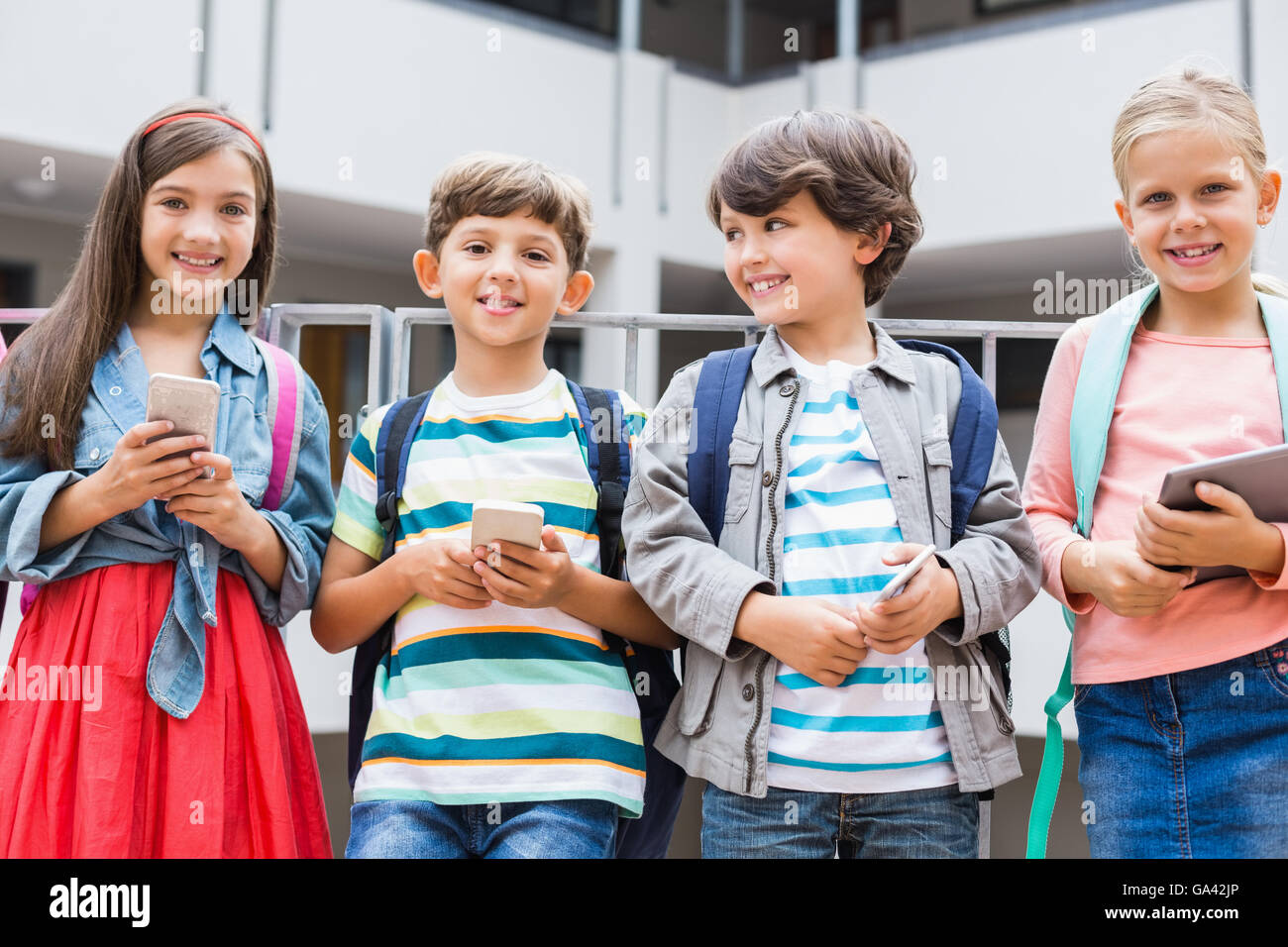 Kids holding mobile phone and digital tablet standing on school terrace ...