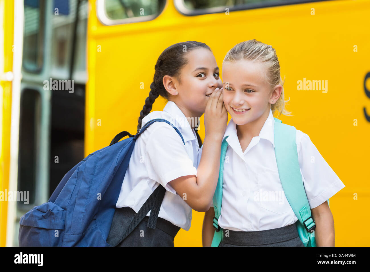 Smiling schoolgirl whispering in her friend's ear Stock Photo