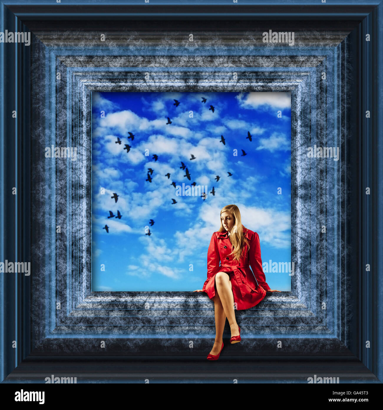 girl in red coat sitting on the edge of a picture frame with birds flying over a blue sky Stock Photo