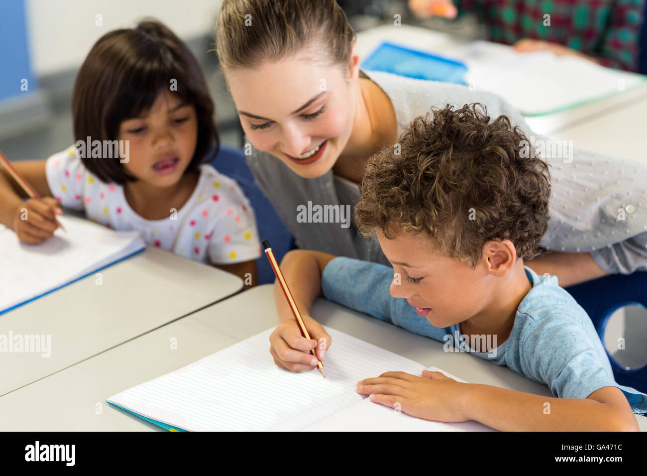 teacher helping schoolchildren to write on book Stock Photo