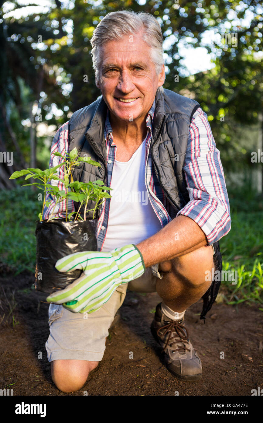 Portrait of happy gardener kneeling with potted plant at garden Stock Photo