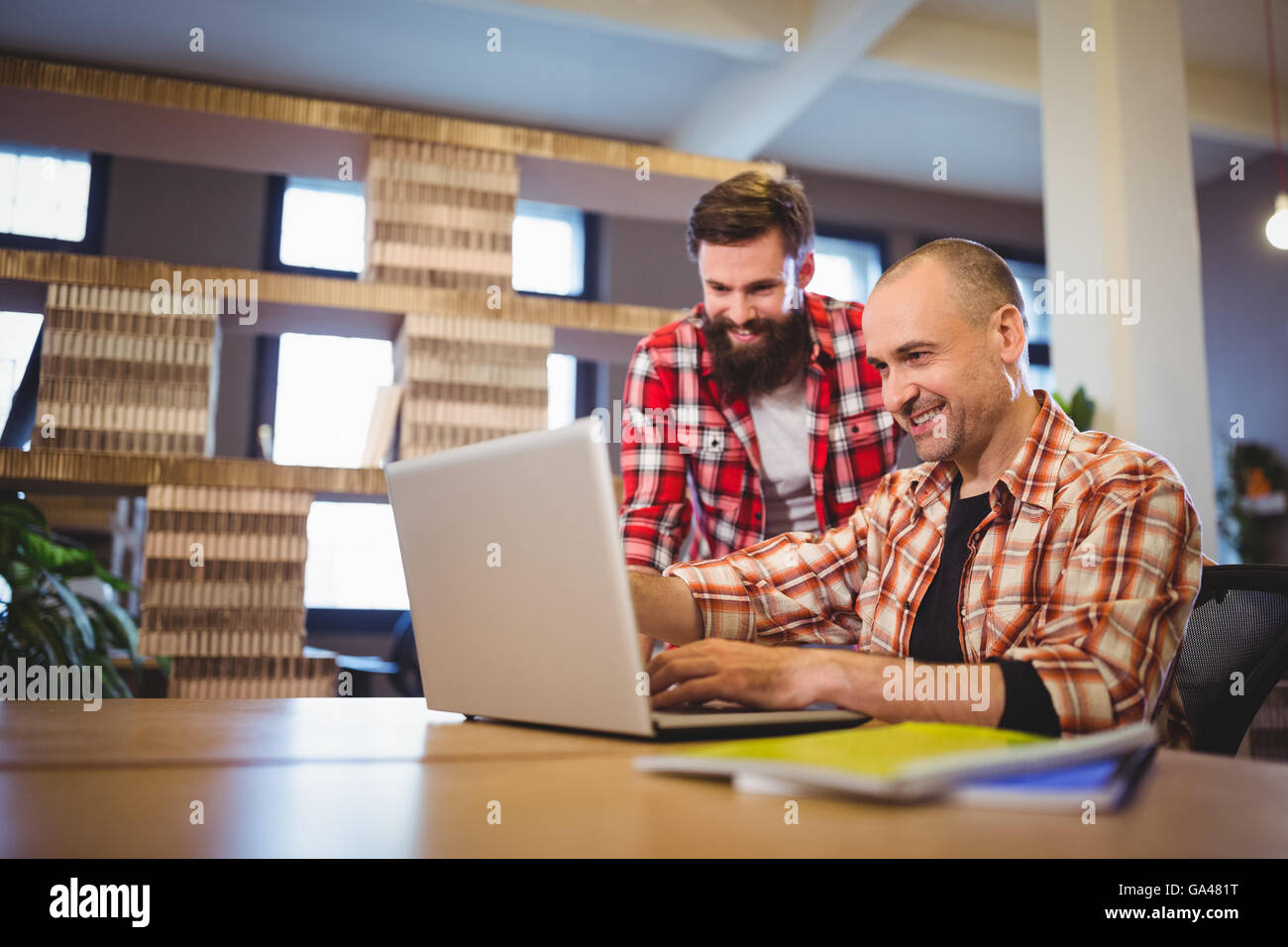 Male colleagues smiling while discussing over laptop Stock Photo