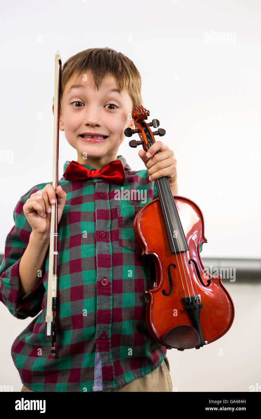 Cute boy holding violin with bow in classroom Stock Photo