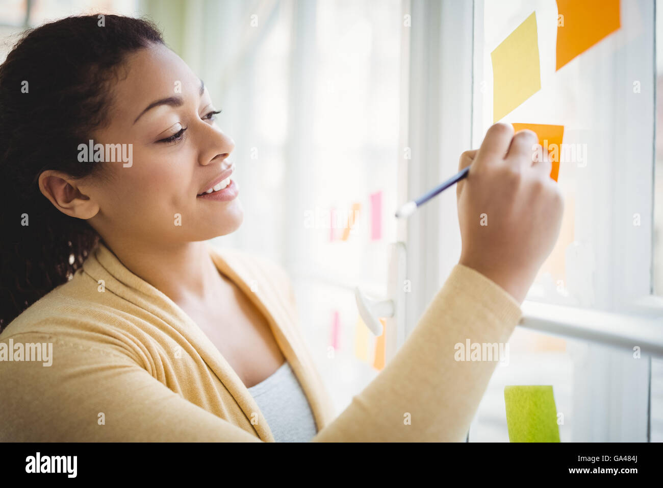 Businesswoman smiling while writing on adhesive note Stock Photo