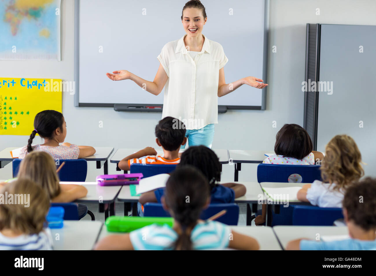 Teacher with arms outstretched in classroom Stock Photo