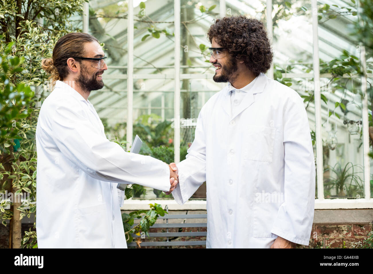 Male scientists handshaking outside greenhouse Stock Photo