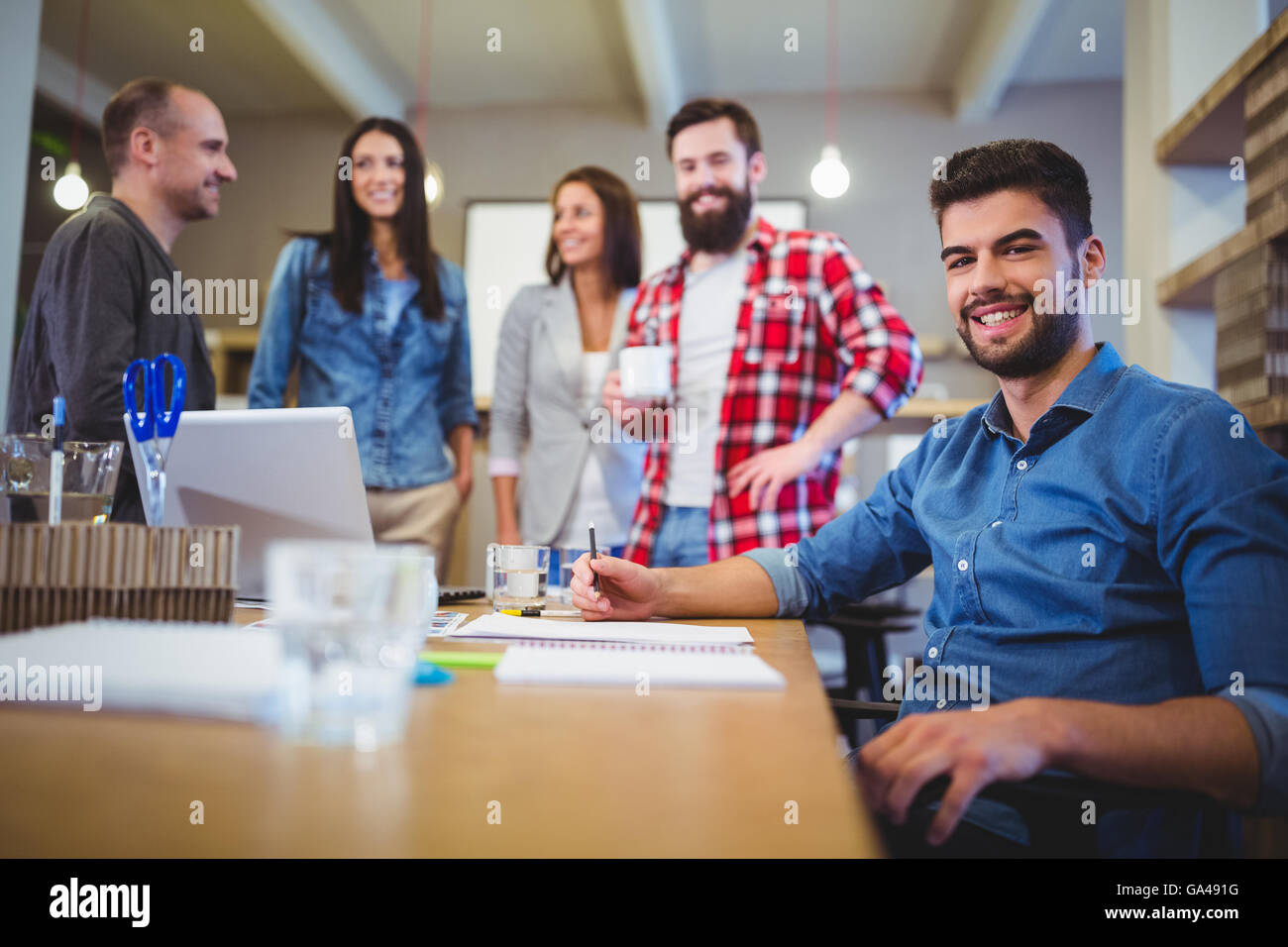 Confident creative businessman with colleagues standing by table Stock Photo