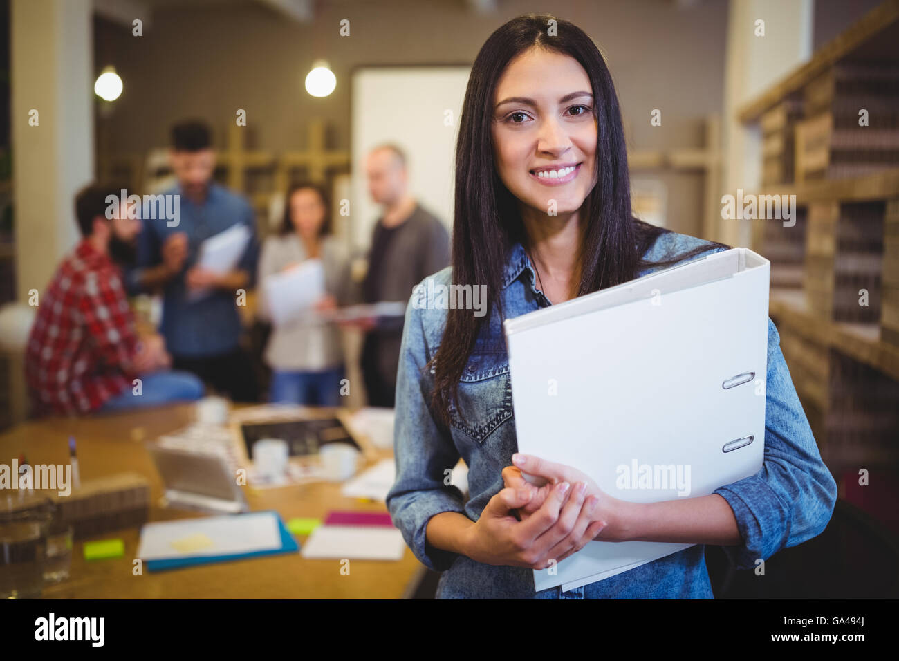 Confident businesswoman holding file while colleagues in background Stock Photo