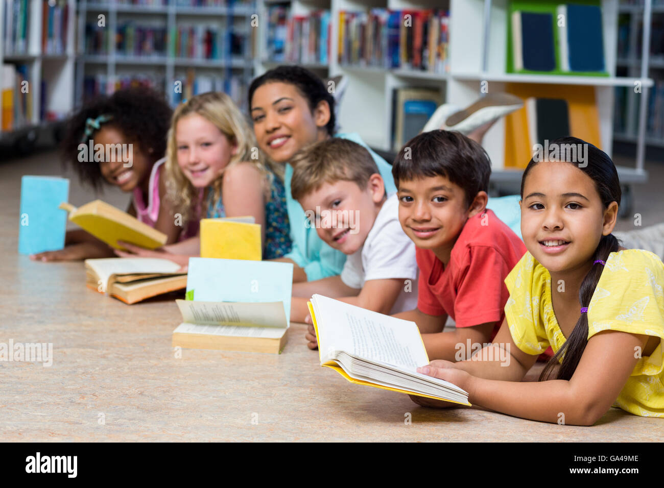 Happy teacher with children lying down while reading books Stock Photo