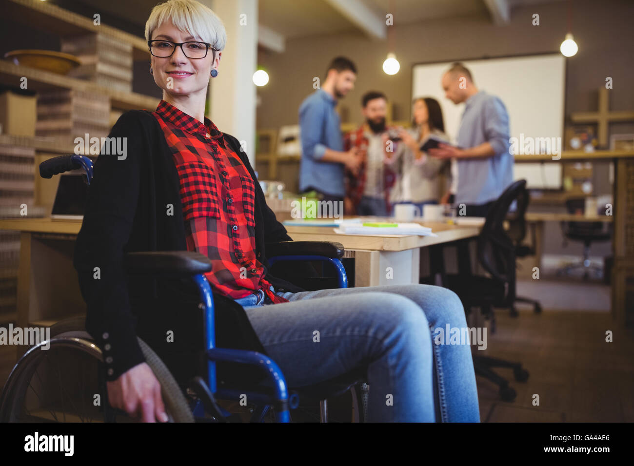Confident woman on wheelchair while colleagues in background Stock Photo
