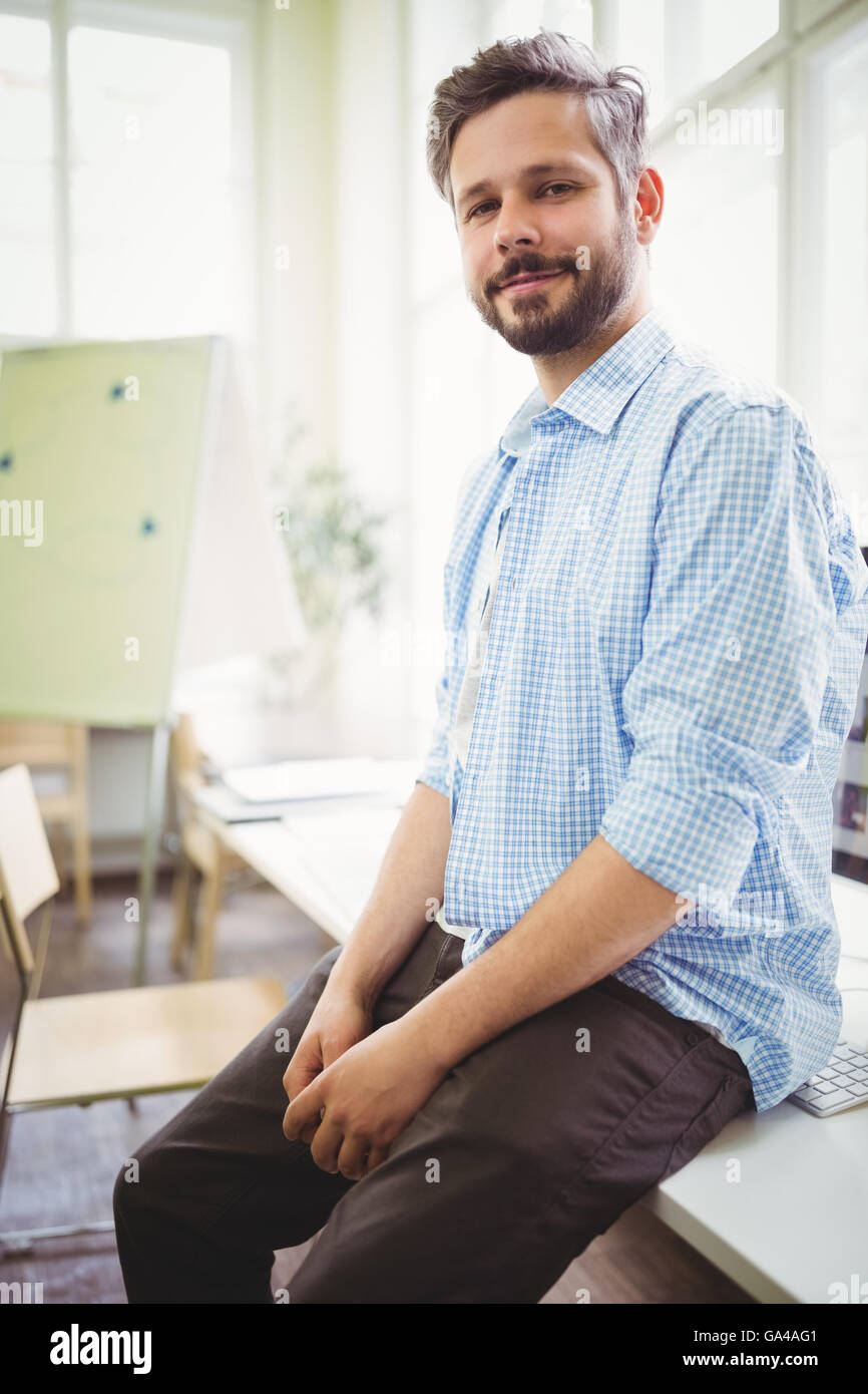 Portrait of smiling businessman sitting on desk in office Stock Photo ...
