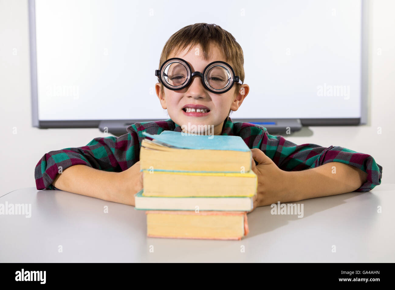 Happy boy holding books on table in classroom Stock Photo