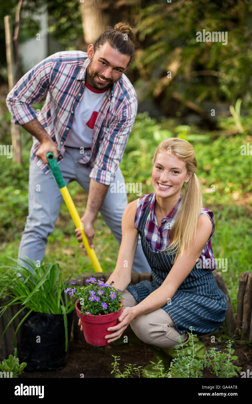 Portrait of happy gardeners with potted plant and shovel at garden ...