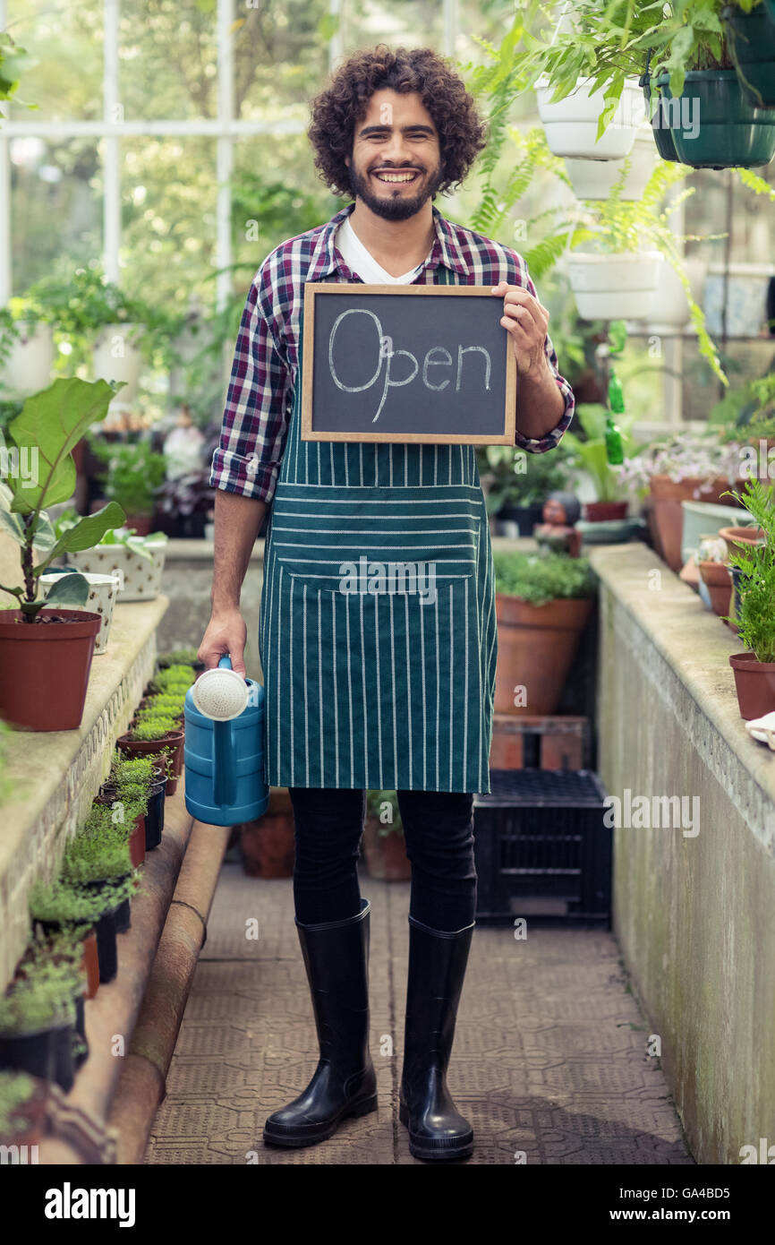 Male gardener holding open sign placard and watering can Stock Photo