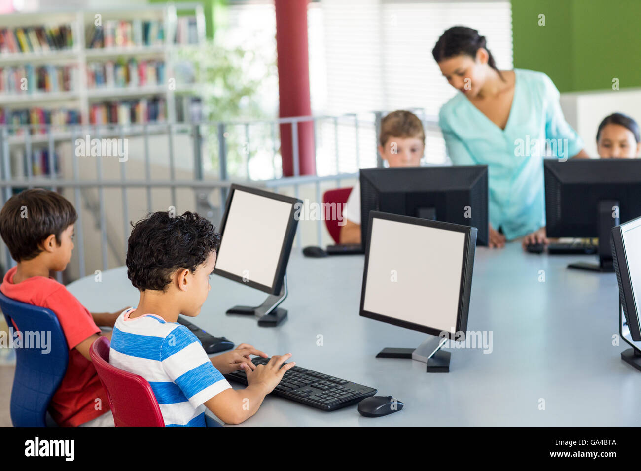 Children using computers as teacher teaching them Stock Photo