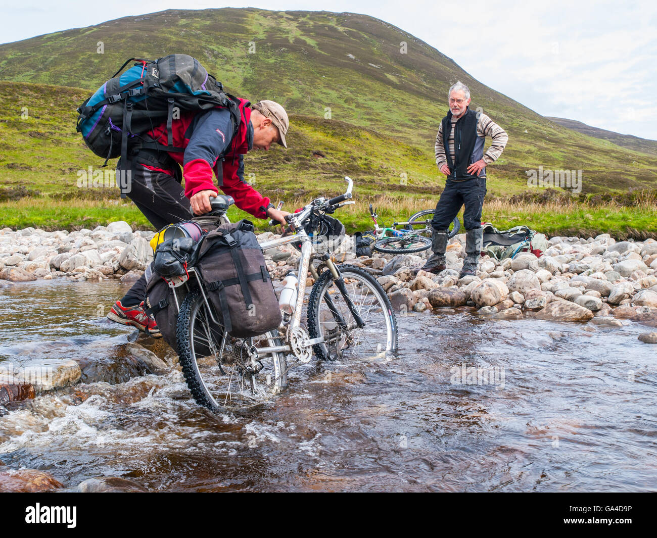 Cyclist fording a river in the Cairngorms, Scotland, whilst on a bike-packing expedition Stock Photo