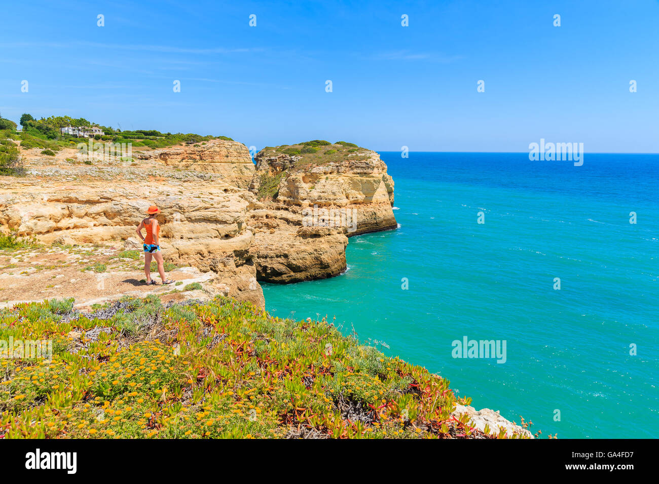 Young woman tourist standing on cliff and looking at beautiful beach near Carvoeiro town, Algarve region, Portugal Stock Photo