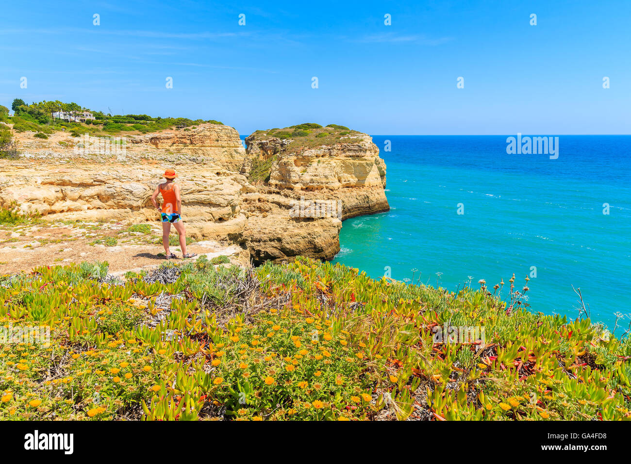 Spring flowers in foreground with young woman tourist standing on cliff rock and looking at sea, Portugal Stock Photo