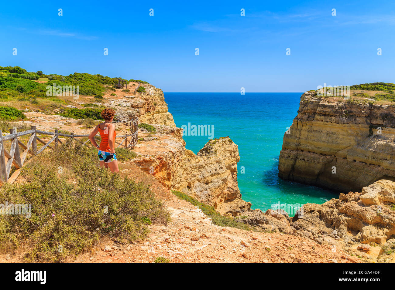 Young woman tourist standing on cliff rock and looking at sea on coast of Portugal, Algarve region Stock Photo