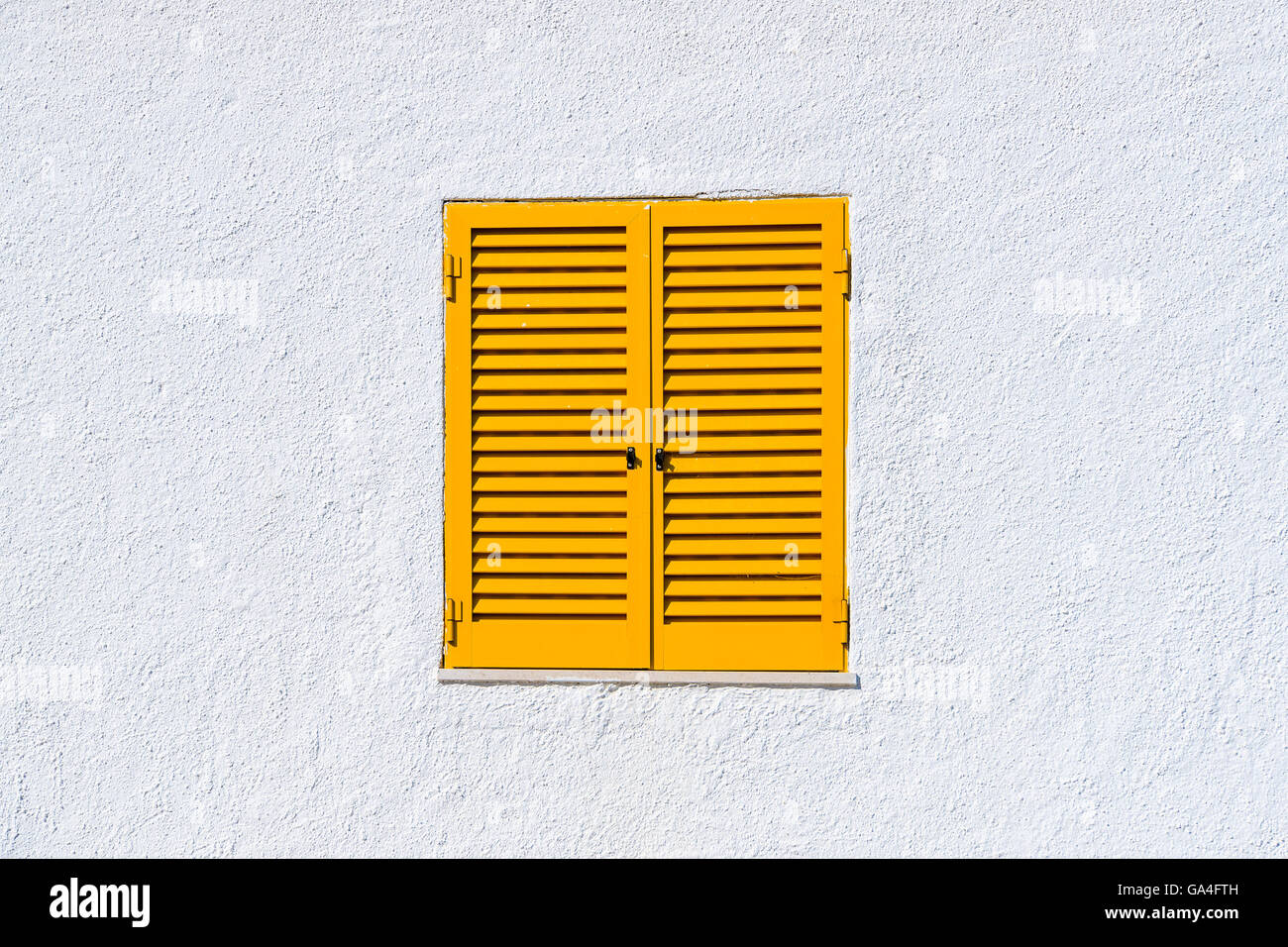 Yellow window shutters and white wall of a house in Luz town, Portugal