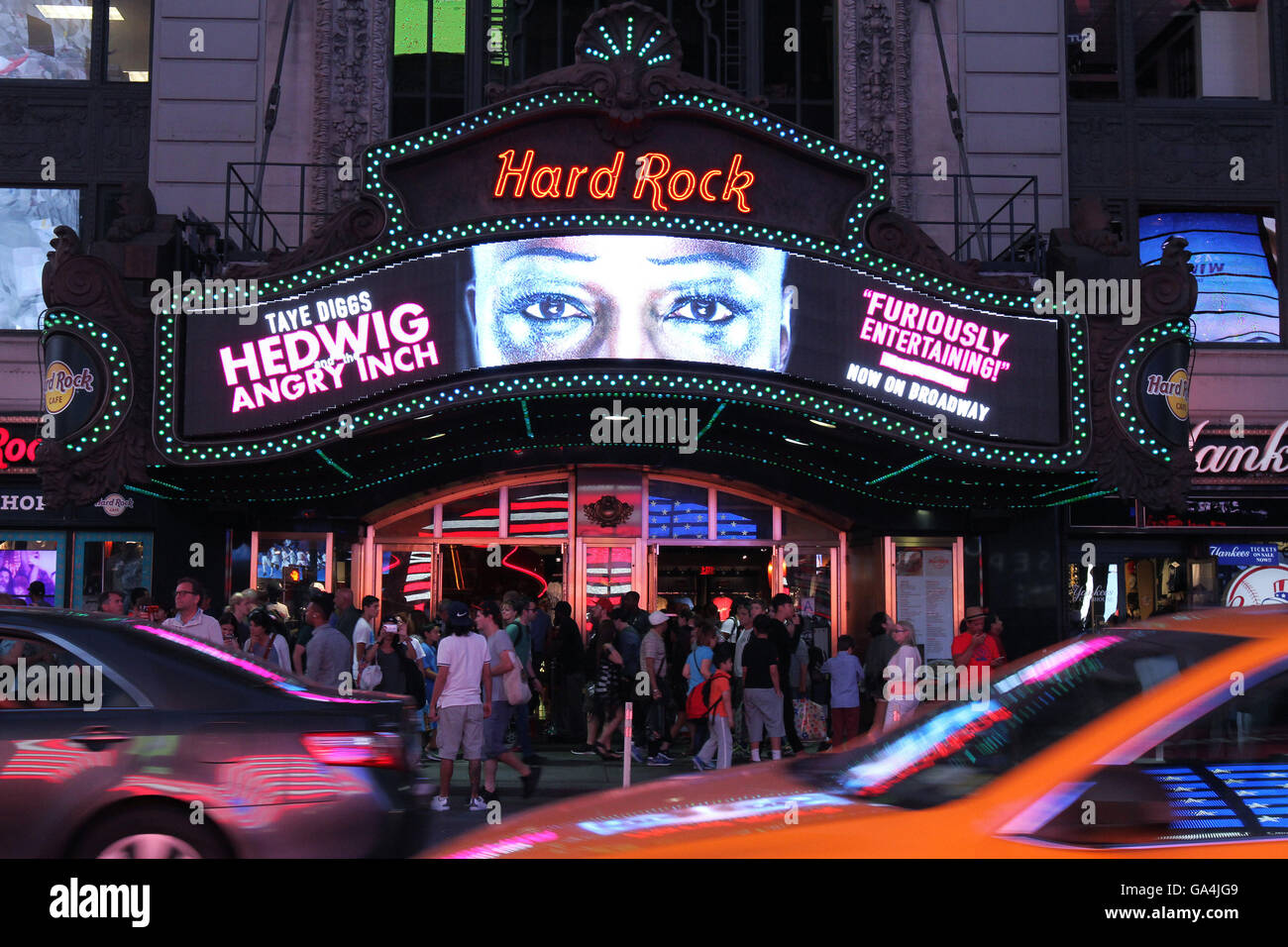 View of tourists at city street entrance to Hard Rock Cafe in midtown New York City near Times Square at dusk during summer. Stock Photo