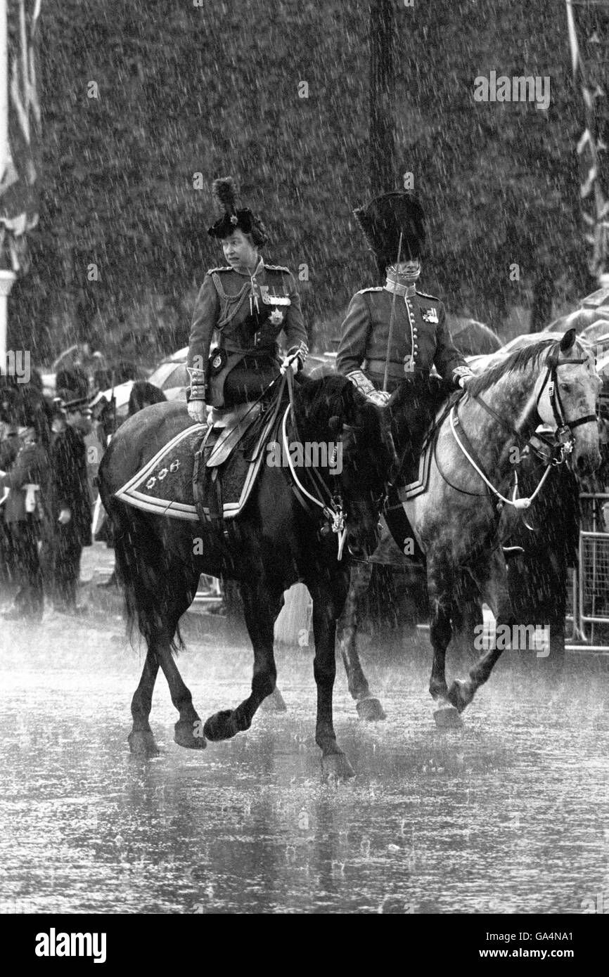 One of the hazards of being a reigning monarch, especially when it's your Birthday Parade, is the unpredictable English weather. After the ceremony of the Trooping of the Colour, Queen Elizabeth II, holding the reins and riding side saddle up on Burmese, canters back to Buckingham Palace, London, in the rain. She will appear on the balcony for the fly-past by the RAF. Stock Photo