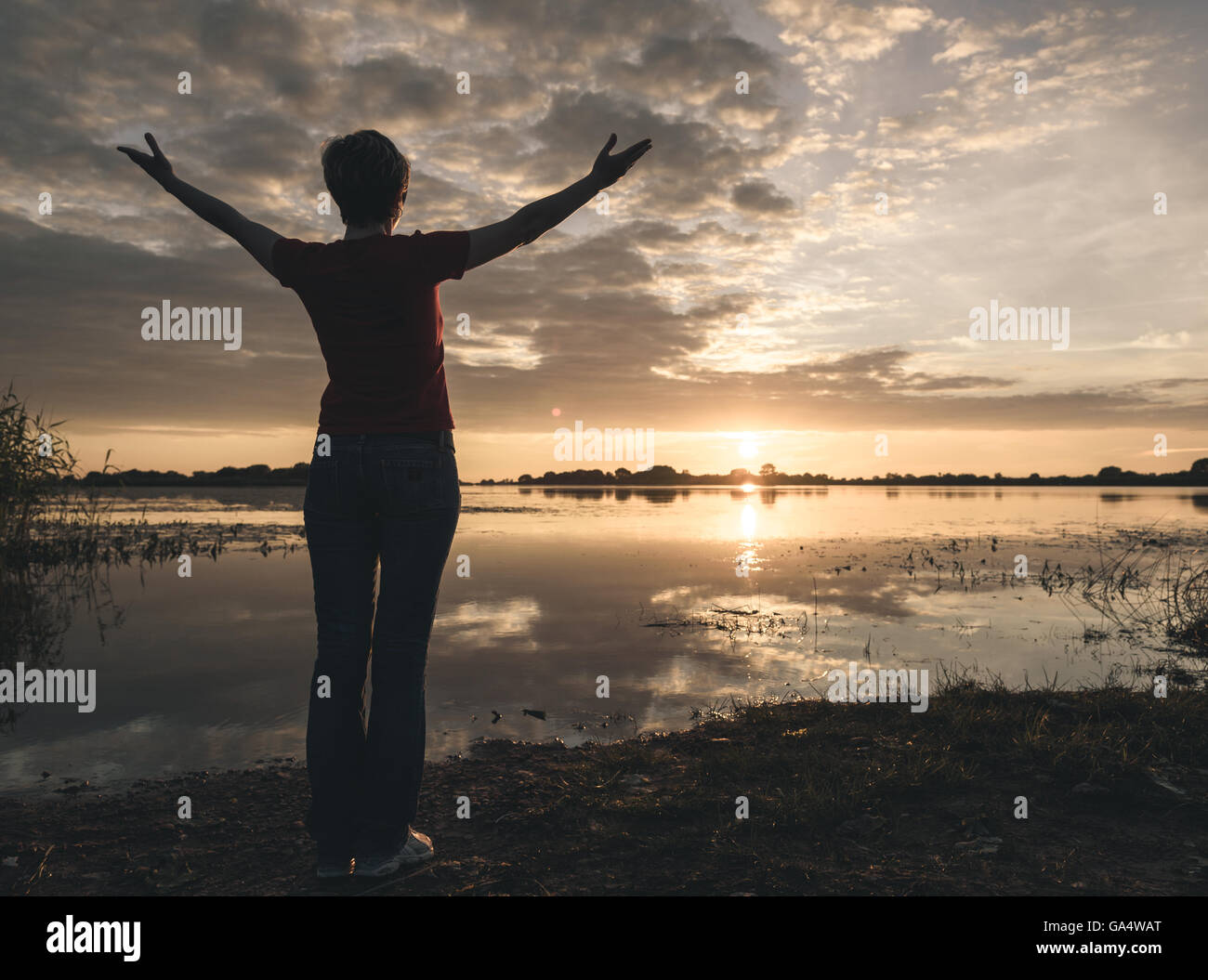 young slim woman meditating onbanks of the lake at sunset Stock Photo