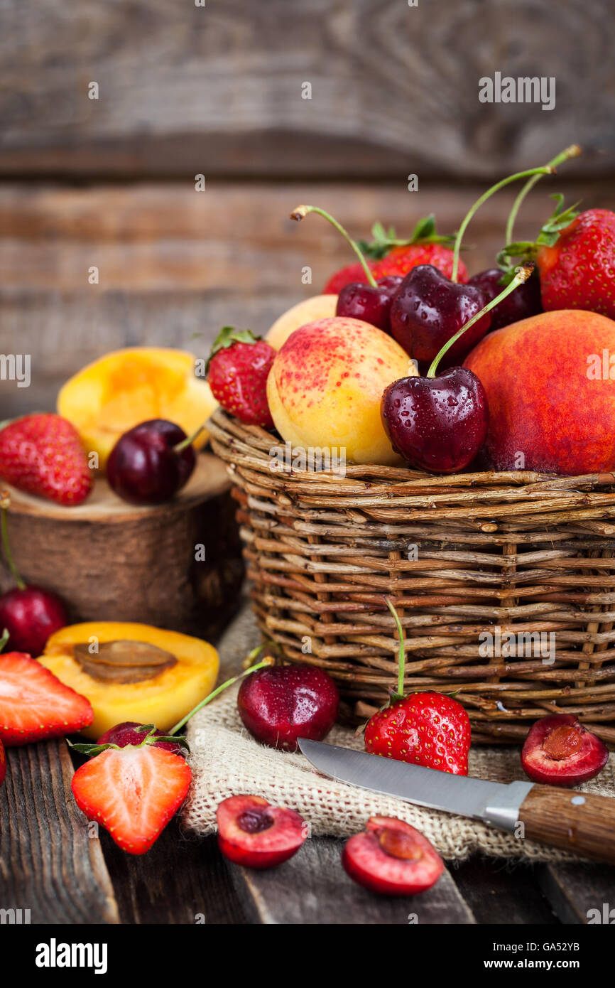 Fresh ripe summer berries and fruits (peaches, apricots, cherry and strawberry) in wicker basket Stock Photo