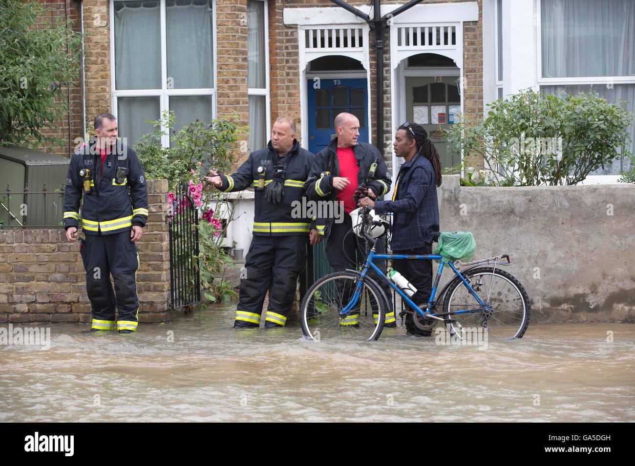 London, UK. 3rd July, 2016. Broken Water Main causes widespread floods in South Wimbledon, London, UK 03.07.2016 Fire services advise a cyclist the safest route outside terraced houses on Kingston Road as water levels rise due to a broken water main in South Wimbledon. Credit:  Jeff Gilbert/Alamy Live News Stock Photo