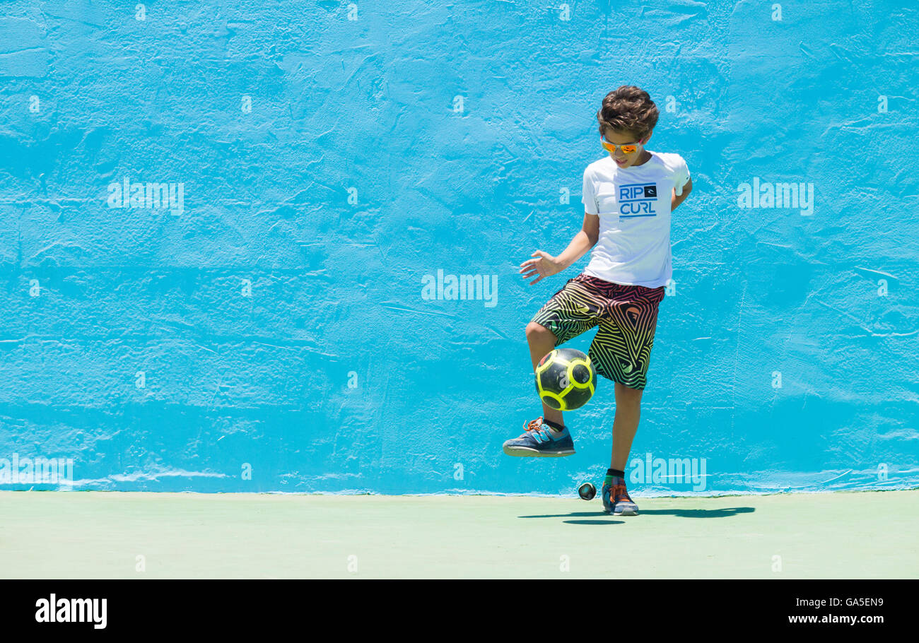 Pozo, Gran Canaria, Canary Islands, Spain, 3rd July 2016. Weather: A boy plays football against a blue wall on the beach in glorious sunshine at the first wave world cup windsurfing event of 2016 at Pozo on the east coast of Gran Canaria. Pozo is famed (and feared by some) for its `nuclear` summer winds, which can exceed 50 knots. The competition takes place between the 3rd - 10th July. Credit:  Alan Dawson News/Alamy Live News Stock Photo