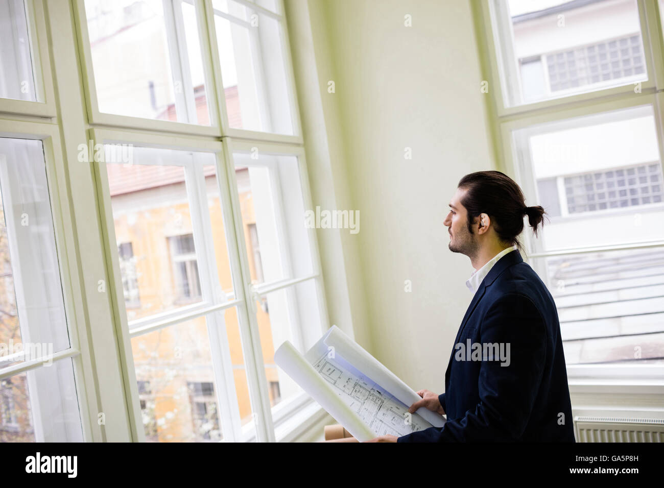 Interior designer holding blueprint while looking through window Stock Photo