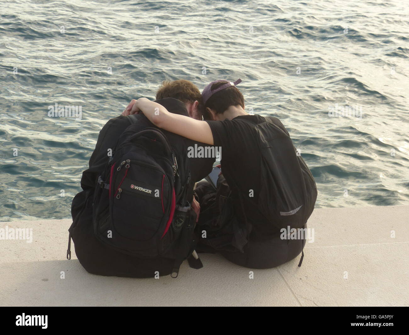 two teenagers sitting by water in embrace late day Zadar Croatia Stock Photo