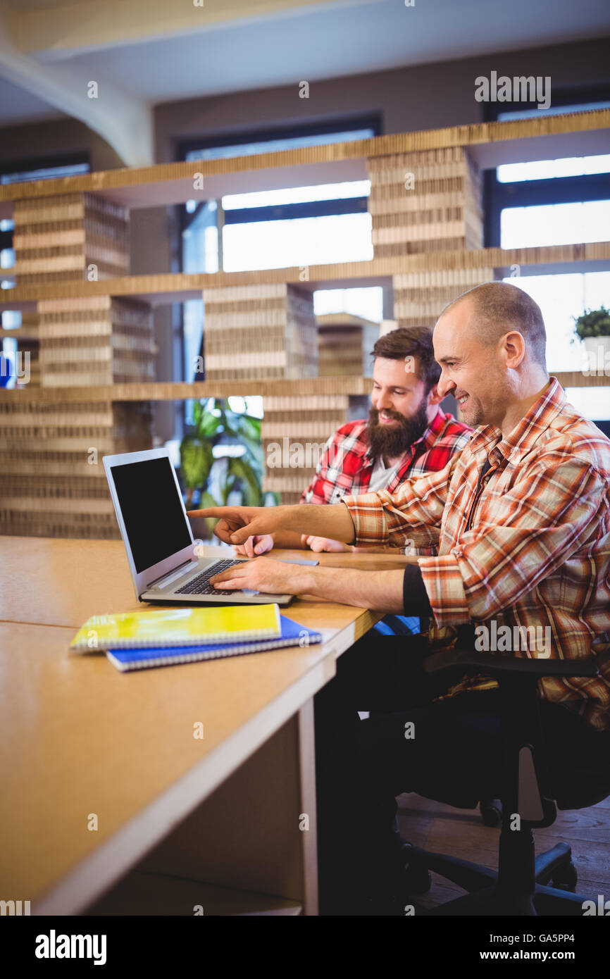 Male colleagues smiling while working with laptop Stock Photo