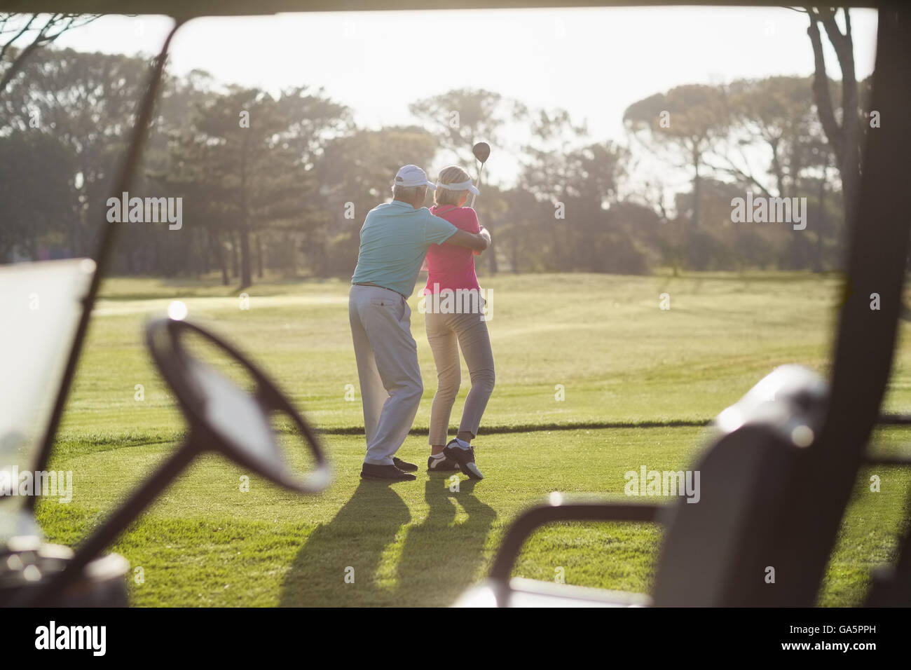 Rear view of mature man teaching woman to play golf Stock Photo