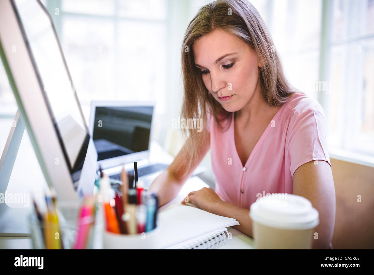 Graphic designer writing on book at desk Stock Photo - Alamy
