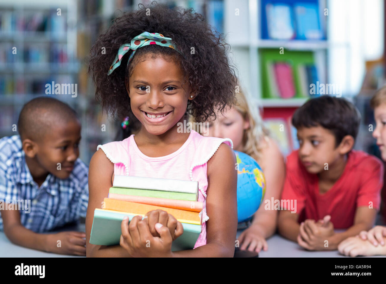 Smiling girl holding books against classmates Stock Photo - Alamy