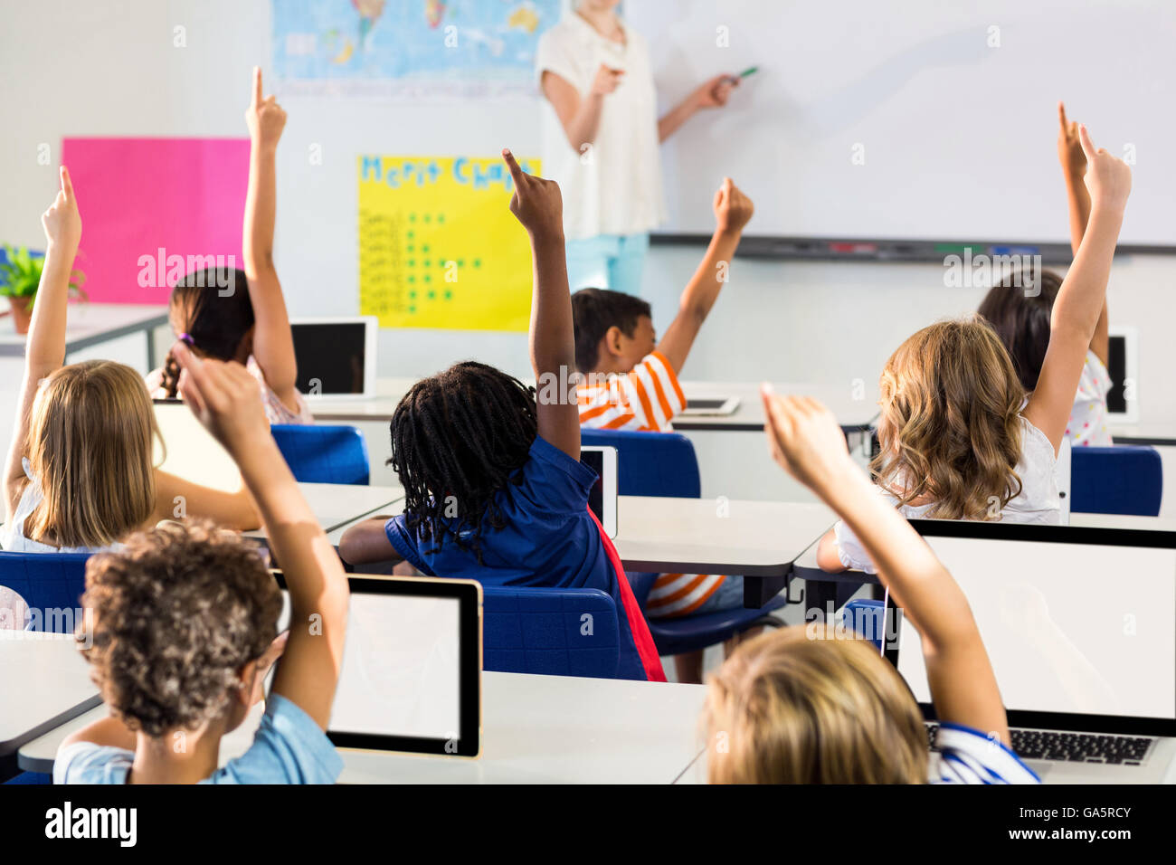 Teacher pointing students with raised hands in classroom Stock Photo