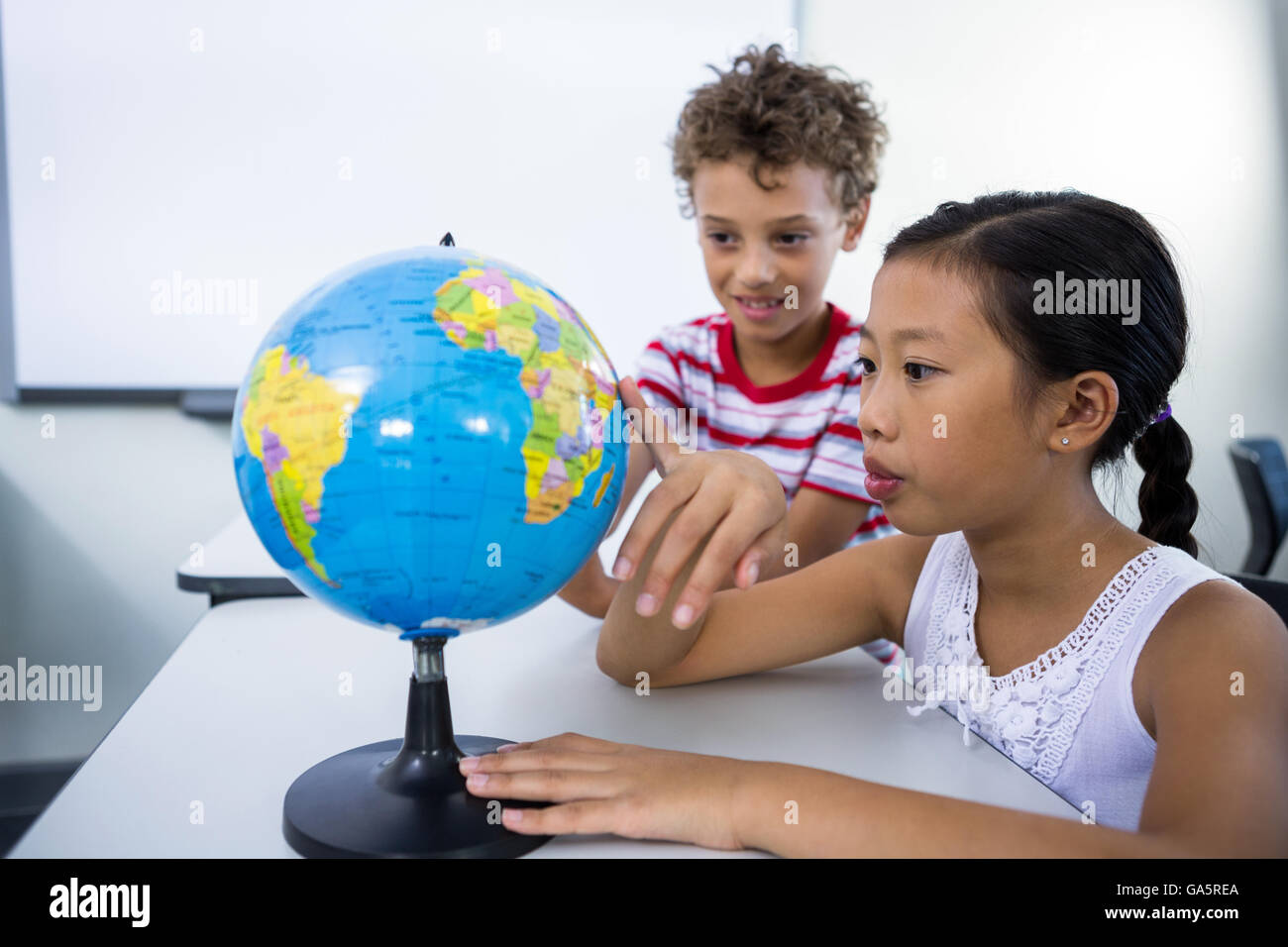 Elementary boy and girl looking at glob in classroom Stock Photo