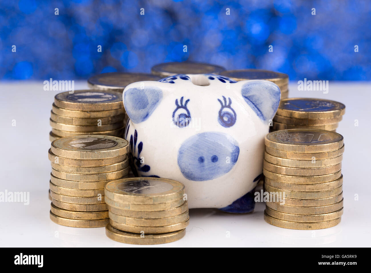 Piggy bank with a stack of coins and a blue blurry background up close ...